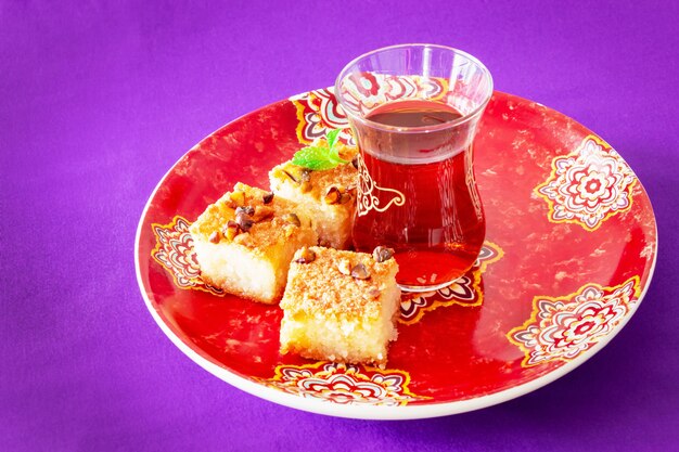 Tee und Piecies Basbousa oder Namoora - traditioneller arabischer süßer Grießkuchen mit Nüssen, Kokosnuss und Orangenblütenwasser. Speicherplatz kopieren. Fliederraum.