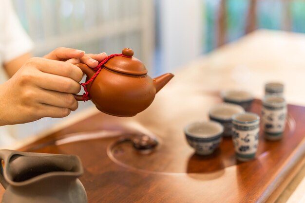 Tee wird in die Cup-Nahaufnahme gegossen. Asiatischer Tee auf Holzbambustisch, Hand sanft gießen