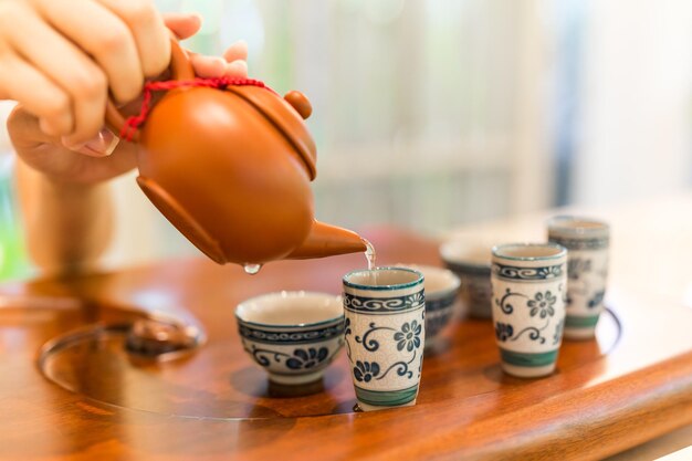 Tee wird in die Cup-Nahaufnahme gegossen. Asiatischer Tee auf Holzbambustisch, Hand sanft gießen