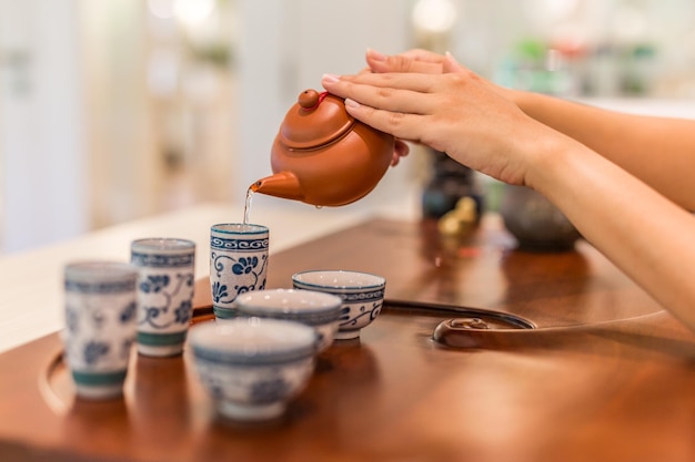 Tee wird in die Cup-Nahaufnahme gegossen. Asiatischer Tee auf Holzbambustisch, Hand sanft gießen