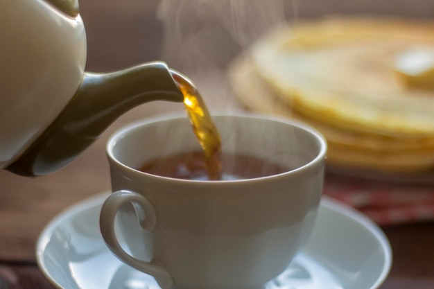 Tee wird in eine Frühstückstasse mit Pfannkuchen gegossen.