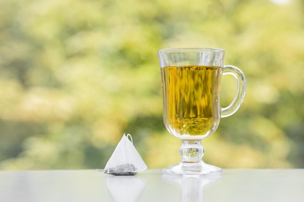 Teebeutel und Tasse Tee auf grünem Sommerhintergrund