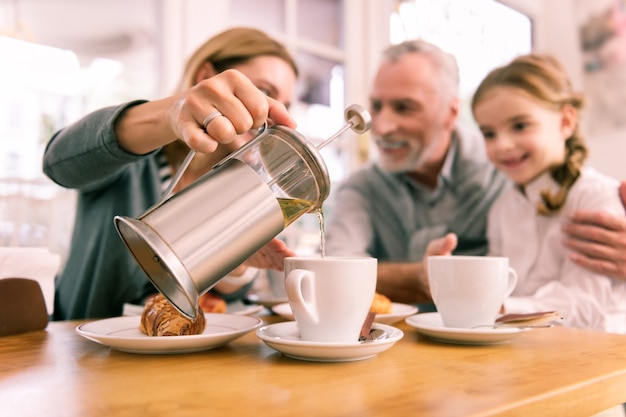 Teekanne. Frau, die kleine Teekanne mit grünem Tee hält, der sie in die Tasse beim Frühstück in der Cafeteria gießt