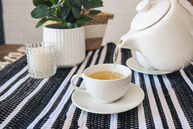 Teekanne gießt Tee in ein Tassentee-Trinkkonzept
