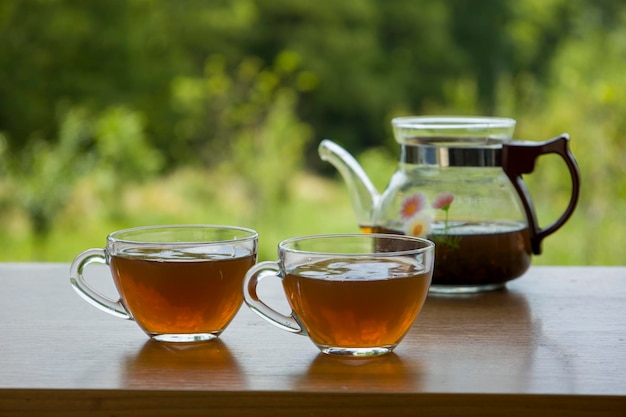 Teekanne mit einer transparenten Tasse Tee in der Natur