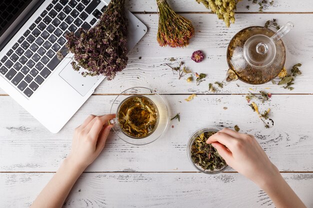 Teekanne mit Kräutertee auf Küchentisch und Frau schreiben Rezept