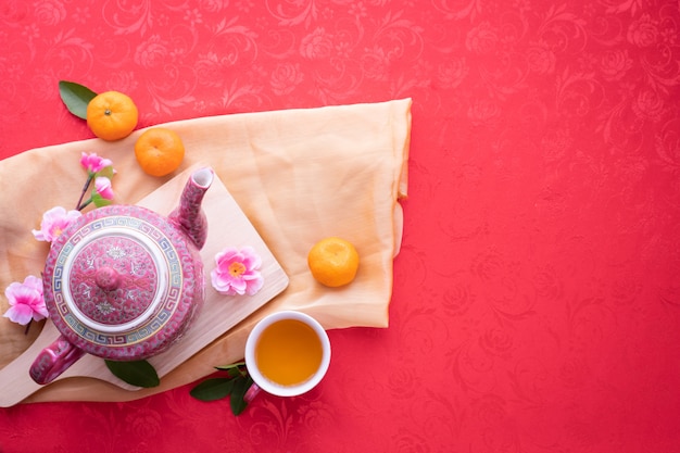 Teekanne und Tasse Tee mit Kirschblüte auf rotem Hintergrund