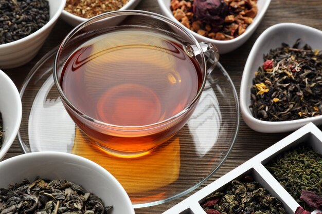 Foto teekonzept verschiedene arten von trockenem tee in keramikschalen glastasse tee auf holzhintergrund in nahaufnahme