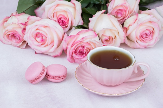 Teemakronen und ein Strauß rosa Rosen auf dem Tisch