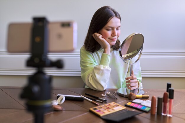 Teen-Blogger mit Schminkspiegel und Make-up, Mädchen, das ihren Abonnenten sagt, was und wie sie Make-up macht, Beauty-Seite auf Blog