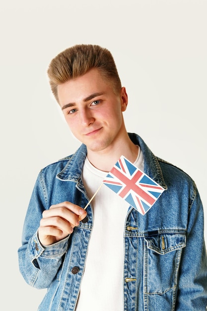 Teen blonder Mann mit weißem T-Shirt und Jeansjacke mit kleiner Flagge Englands, während er auf dem weißen Hintergrund steht