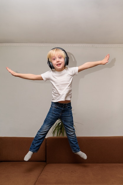 Teen Boy, der Musik auf Kopfhörern hört und auf Couch springt.