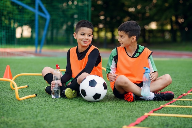 Teen Boys in Fußballuniformen, die sich auf dem Sportplatz ausruhen.