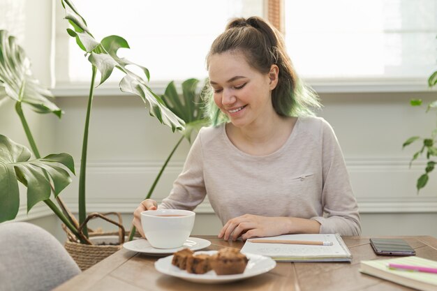 Teen Girl isst Cupcakes, trinkt Tee und sitzt am Tisch