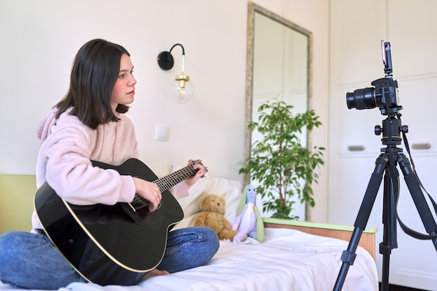 Teen mädchen sitzen zu hause im bett mit einer akustikgitarre, mädchen lernen, die gitarre online zu spielen. technologie, soziale netzwerke, kunst, hobby, jugendkonzept