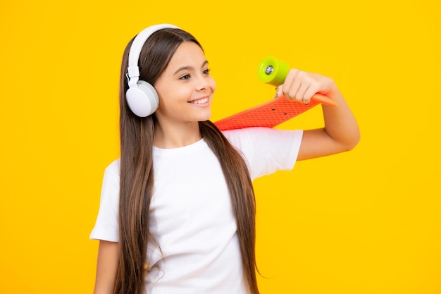 Teen Schule Mädchen mit Skateboard und Kopfhörer auf Studio isoliert Hintergrund Frühling Schulmädchen Trend urbanen Teenager-Stil Glückliches Teenager-Porträt Lächelndes Mädchen