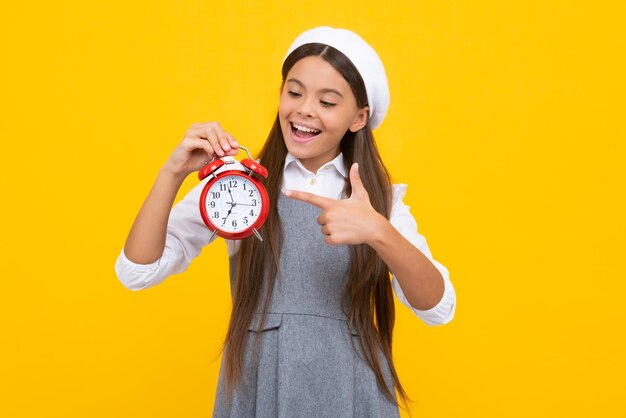 Teen Student Mädchen halten Uhr isoliert auf gelbem Hintergrund Zeit zur Schule Teenager-Kind mit Wecker zeigt Zeit spätes Erwachen Glückliches Mädchen Gesicht positive und lächelnde Emotionen