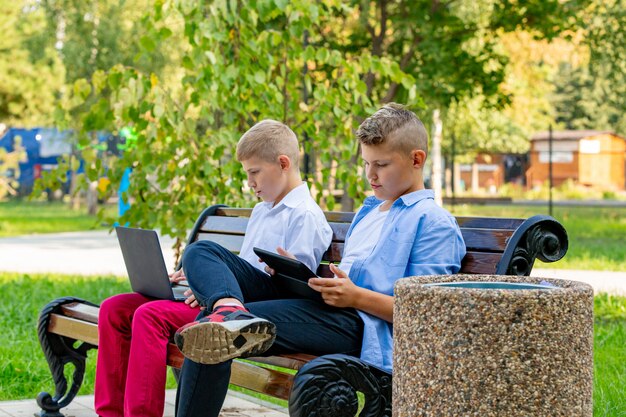 Teenager auf Parkbank mit Laptop und digitalem Tablet