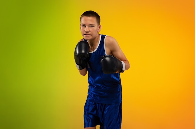 Teenager-Boxer gegen Gradienten-Neon-Studio-Hintergrund in Bewegung des Kickboxens