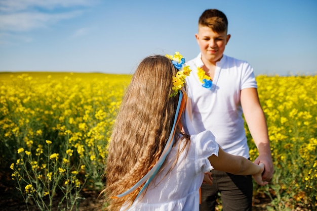 Teenager Bruder und Schwester mit ukrainischem Kranz auf dem Kopf im Rapsfeld unter blauem Himmel