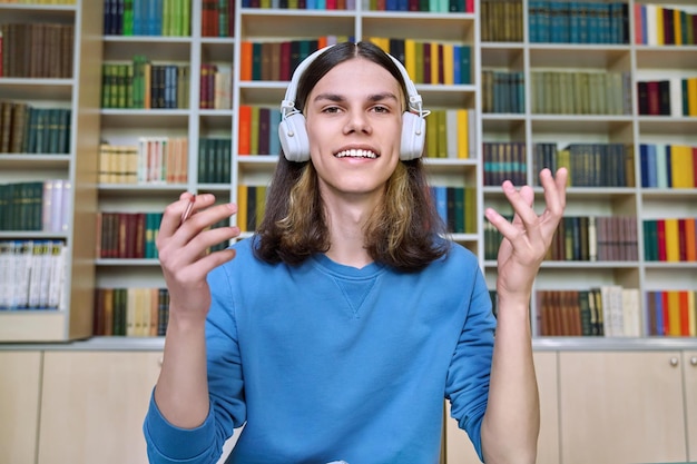 Teenager-College-Student mit Kopfhörern, der die Webcam am Schreibtisch in der Bibliothek anschaut