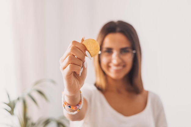 Teenager, der einen virtuellen goldenen Bitcoin mit seiner Hand hält und ihn der Kamera zeigt, lächelt und Spaß hat.