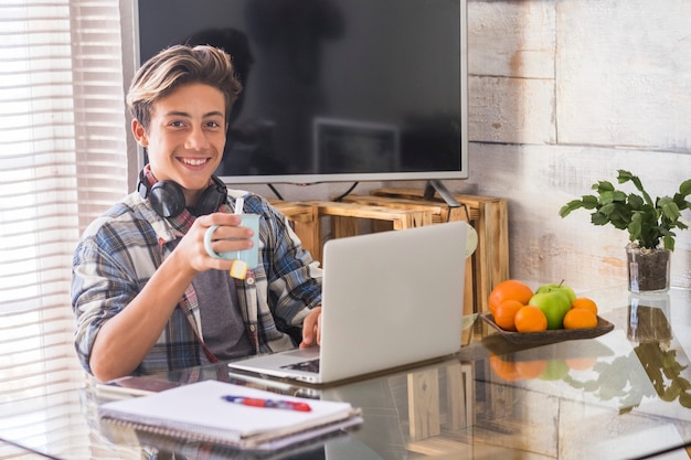 Teenager, der Hausaufgaben mit Laptop und zu Hause macht - Innen- und Lernkonzept - Kerl, der die Kamera anschaut und lächelt