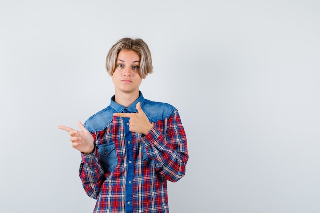 Foto teenager, der im karierten hemd auf die linke seite zeigt und fokussiert aussieht. vorderansicht.