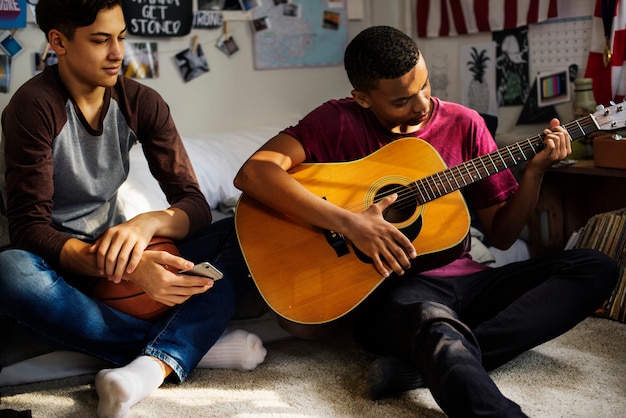 Teenager, die heraus in einem Schlafzimmer hängen, ein Hobby- und Musikkonzept der Akustikgitarre spielend