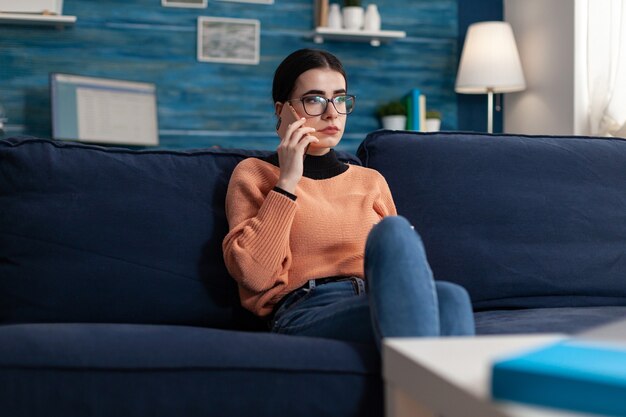 Teenager diskutieren am Telefon über die Universitätsprüfung, während sie auf dem Sofa im Wohnzimmer liegen. Schüler, der während der Coronavirus-Quarantäne auf dem Smartphone über Internettechnologie spricht, gelegentliches Klatschgespräch