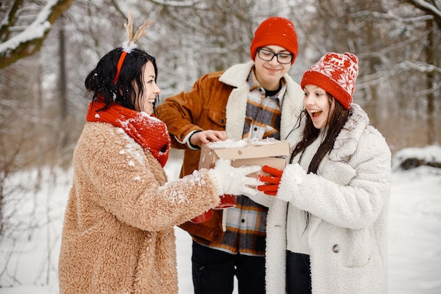 Teenager-Geschwister und ihre Mutter stehen mit einer Geschenkbox im Winterpark