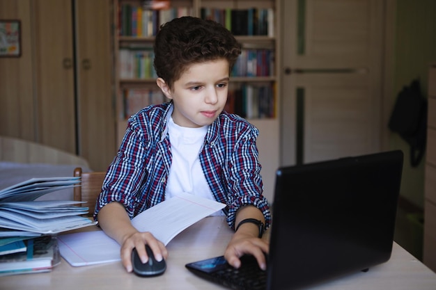 Teenager-Junge an einem Tisch mit einem Laptop arbeitet mit einer Maus und schaut auf den Monitor Coronavirus unter Quarantäne Heimunterricht Selektiver Fokus Unscharfer Hintergrund