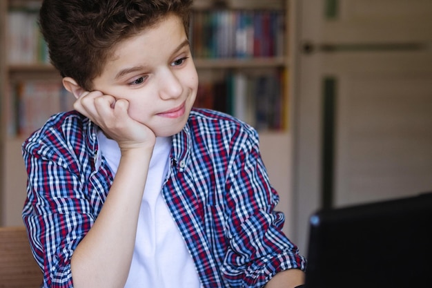 Teenager-Junge an einem Tisch mit einem Laptop schaut in den Monitor, der seinen Kopf mit der Hand stützt Coronavirus unter Quarantäne gestellte Heimschule Selektiver Fokus Unscharfer Hintergrund