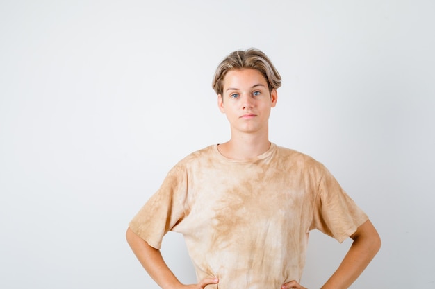 Teenager-Junge, der die Hände im T-Shirt an der Taille hält und selbstbewusst aussieht. Vorderansicht.
