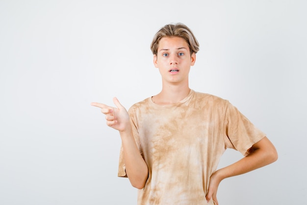 Teenager-Junge im T-Shirt nach links zeigend und enttäuscht, Vorderansicht.