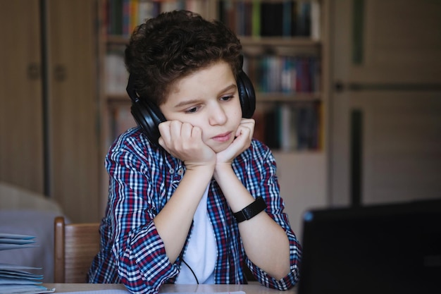 Teenager-Junge mit Kopfhörern hört nachdenklich Musik, die am Tisch sitzt Training zu Hause auf Coronavirus-Quarantäne Selektiver Fokus Hintergrund verwischen