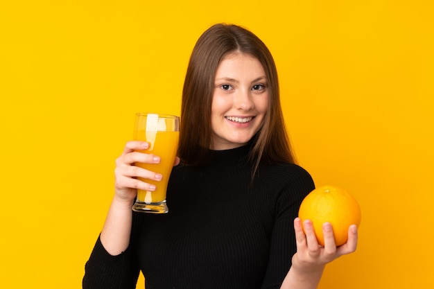 Teenager kaukasisches Mädchen, das eine Orange über isoliertem Gelb hält
