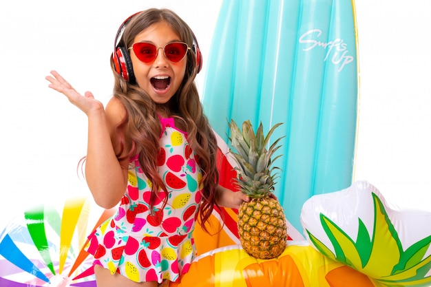 Teenager kaukasisches Mädchen in der Sonnenbrille mit Ananas und Gummimatratzen auf weißer Wand