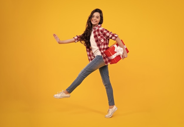 Teenager-Kind im T-Shirt mit Geschenkbox auf gelbem, isoliertem Hintergrund Geschenk für Kindergeburtstag Glücklicher Teenager positive und lächelnde Emotionen von Teenager-Mädchen