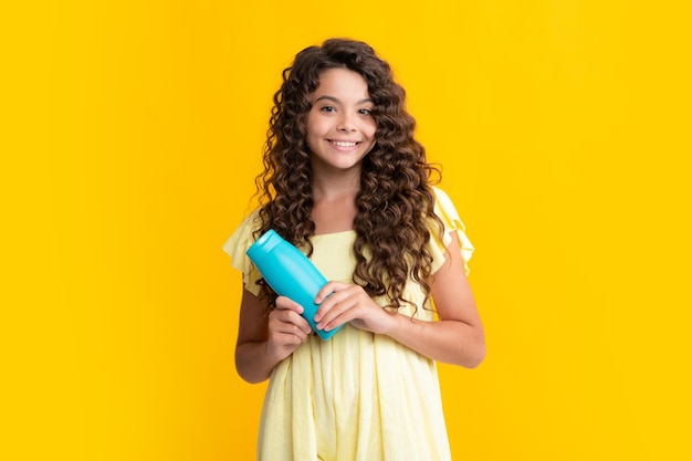 Teenager-Kind-Mädchen zeigt Flasche Shampoo Conditioner oder Duschgel isoliert auf gelbem Hintergrund Haarkosmetikprodukt Mock-up-Flasche Glückliches Teenager-Porträt Lächelndes Mädchen