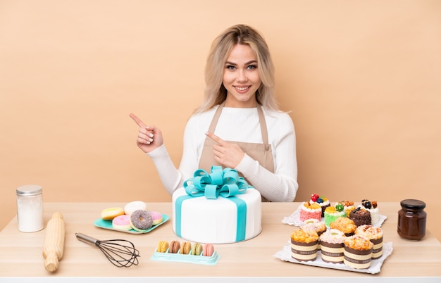 Teenager-Konditor mit einem großen Kuchen in einem Tisch, der Finger zur Seite zeigt