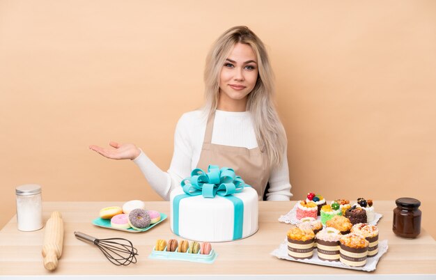 Teenager-Konditor mit einem großen Kuchen in einem Tisch, der imaginären Copyspace auf der Handfläche hält