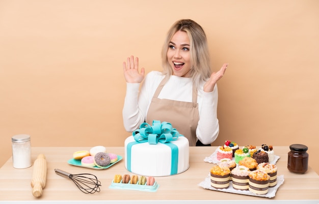 Teenager-Konditor mit einem großen Kuchen in einem Tisch mit überraschendem Gesichtsausdruck