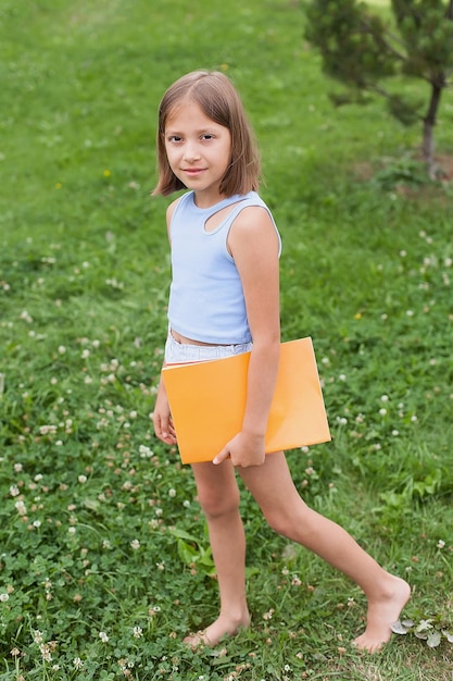 Teenager-Mädchen 8-9 Jahre alt, Sommerpark hält Notizbücher, Ordner-Lehrbücher in den Händen. Restschule, College, Serious Look, Freiraum-Kopiertext. Wissenstraining, Erziehungswissenschaft.