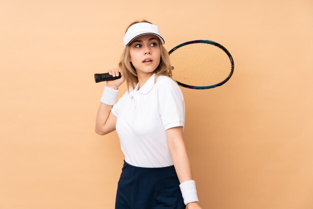 Teenager-Mädchen auf beige Wand, die Tennis spielt
