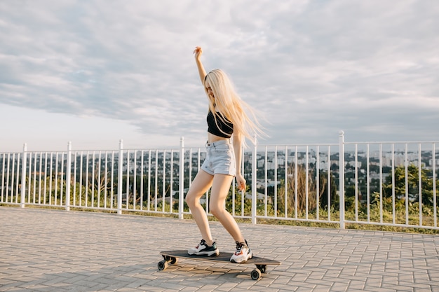 Teenager-Mädchen auf einem Longboard, draußen bei Sonnenuntergang