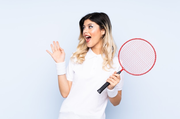 Teenager-Mädchen, das Badminton auf blauer Wand mit überraschtem Gesichtsausdruck spielt