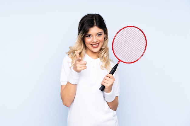 Teenager-Mädchen, das Badminton auf blauer Wand spielt, zeigt Finger auf Sie