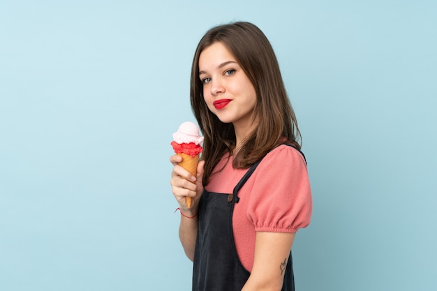 Teenager-Mädchen, das ein Kornett-Eis auf blauer Wand hält