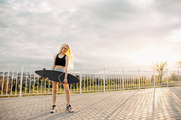 Teenager-Mädchen, das ein Longboard hält, draußen bei Sonnenuntergang